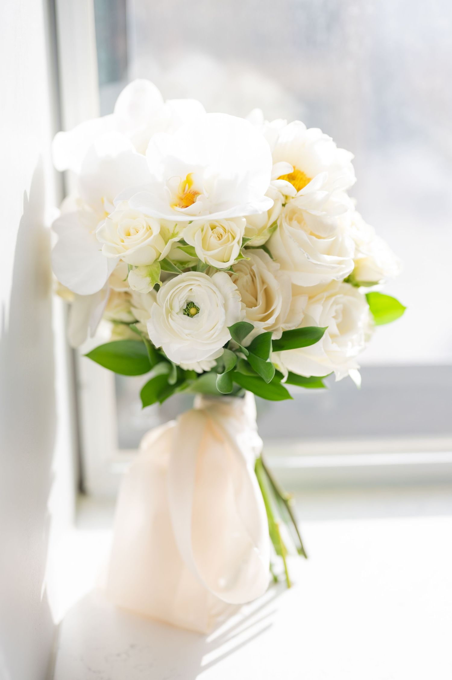 Stunning white bridal bouquet with roses, orchids and ranunculus tied with a blush ribbon.