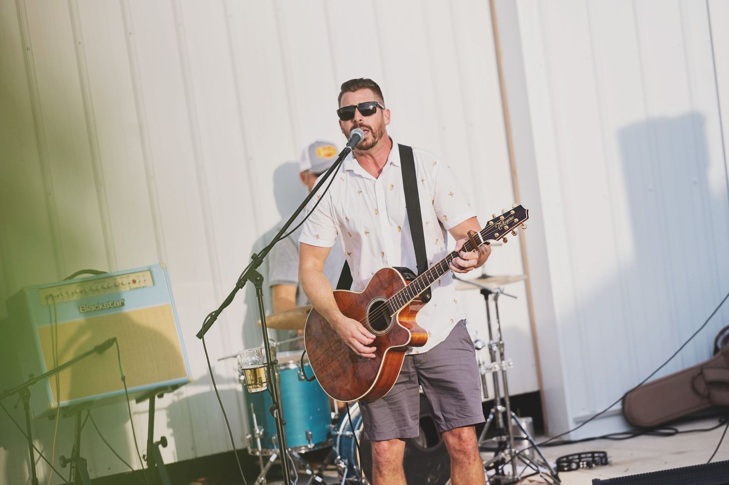 A musician performs on stage with an acoustic guitar and microphone during an outdoor concert.
