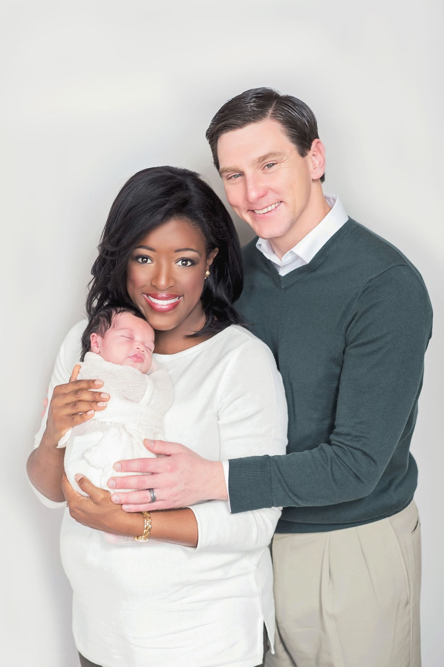 A couple in white and dark clothing poses together holding a baby in three similar studio portraits.