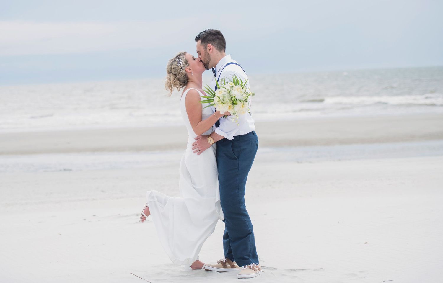 Wedding couple embracing on sandy beach with ocean waves in background.