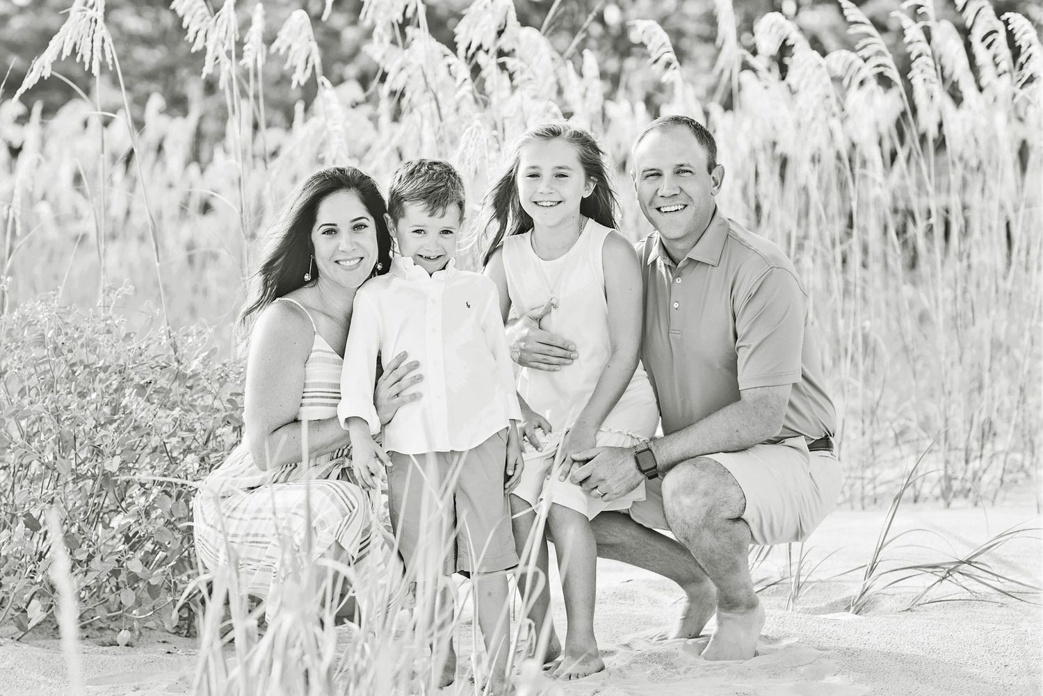 Hilton Head family poses together outdoors in black and white among tall beach grass on a sunny day.