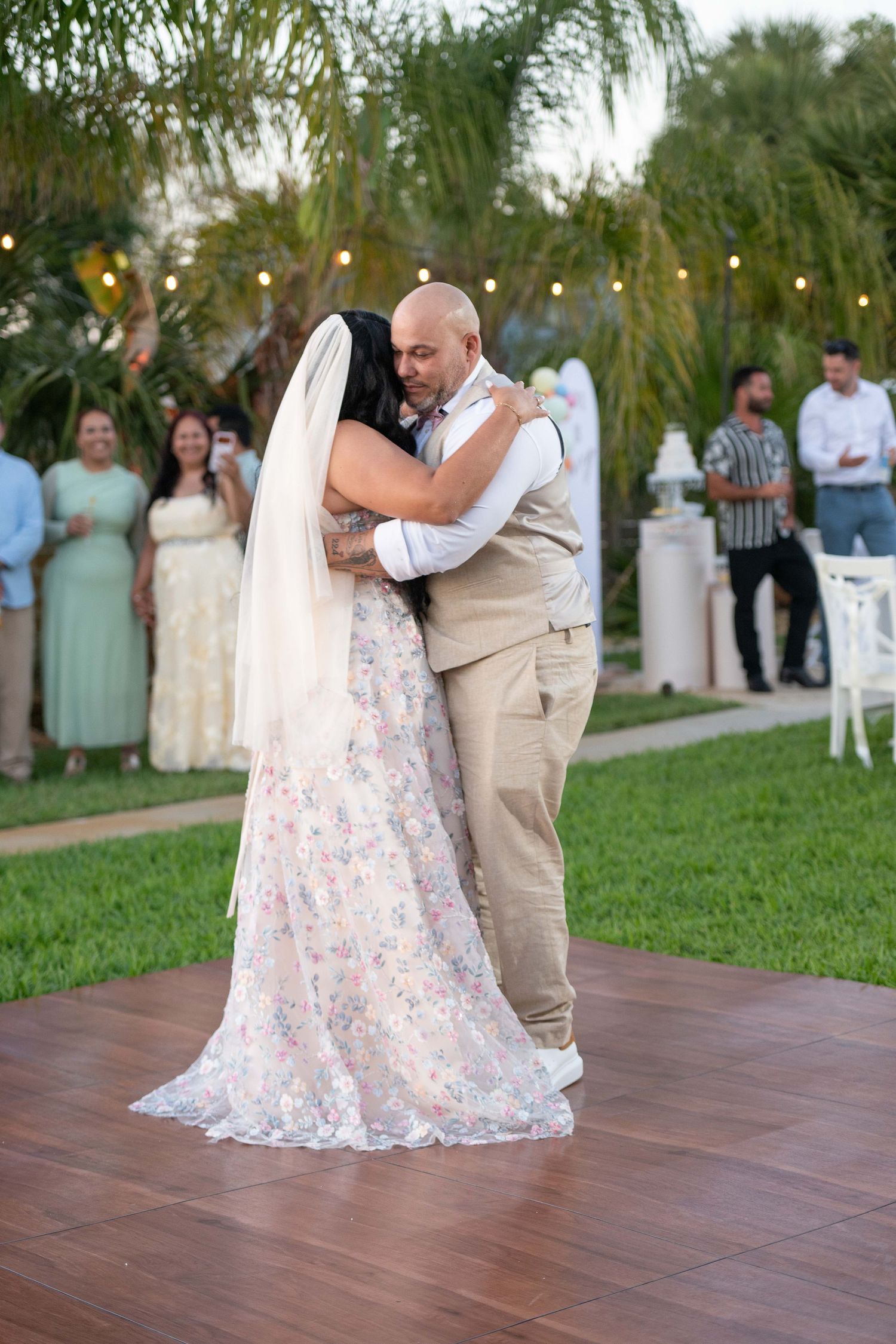 Bride and groom share their first dance outdoors on a wooden floor at a garden wedding reception.