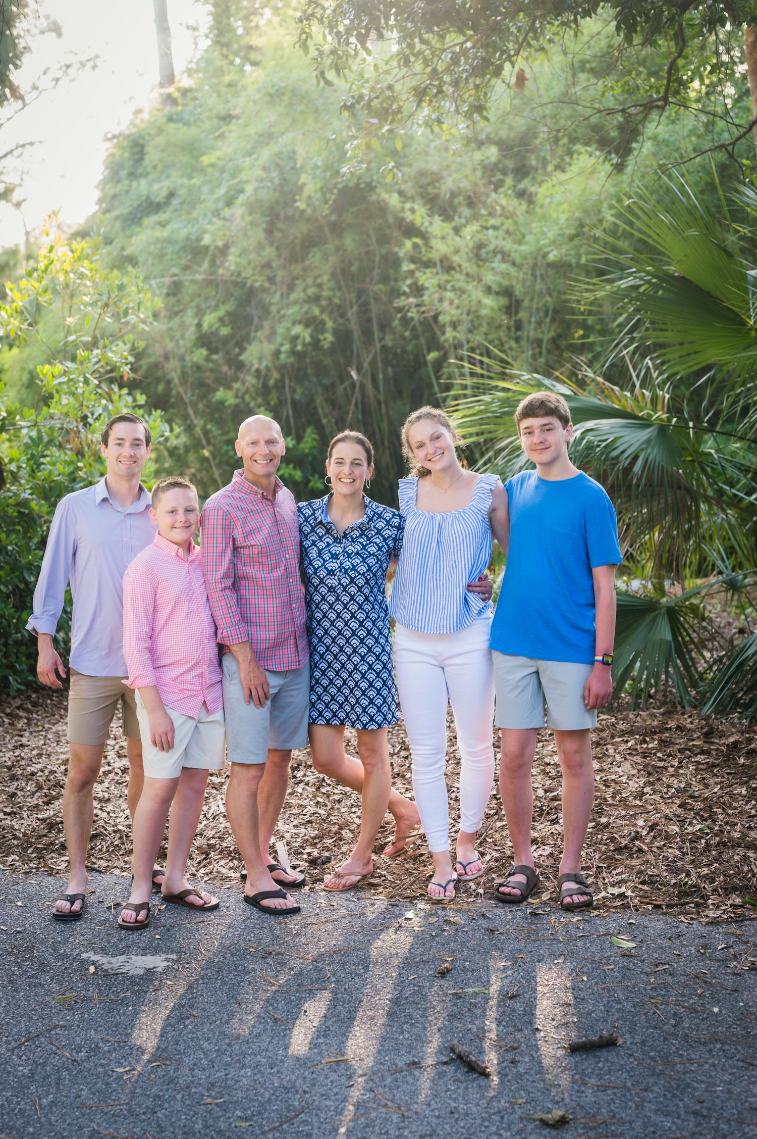 Children in coordinating pastel outfits pose together on a path lined with palm trees and greenery.