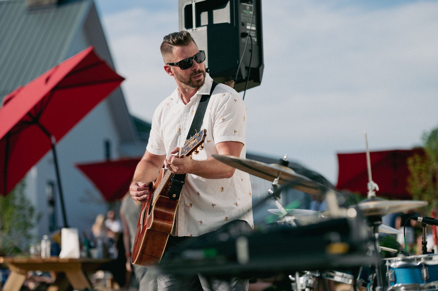 A musician performs on stage with an acoustic guitar at an outdoor venue during a sunny day.