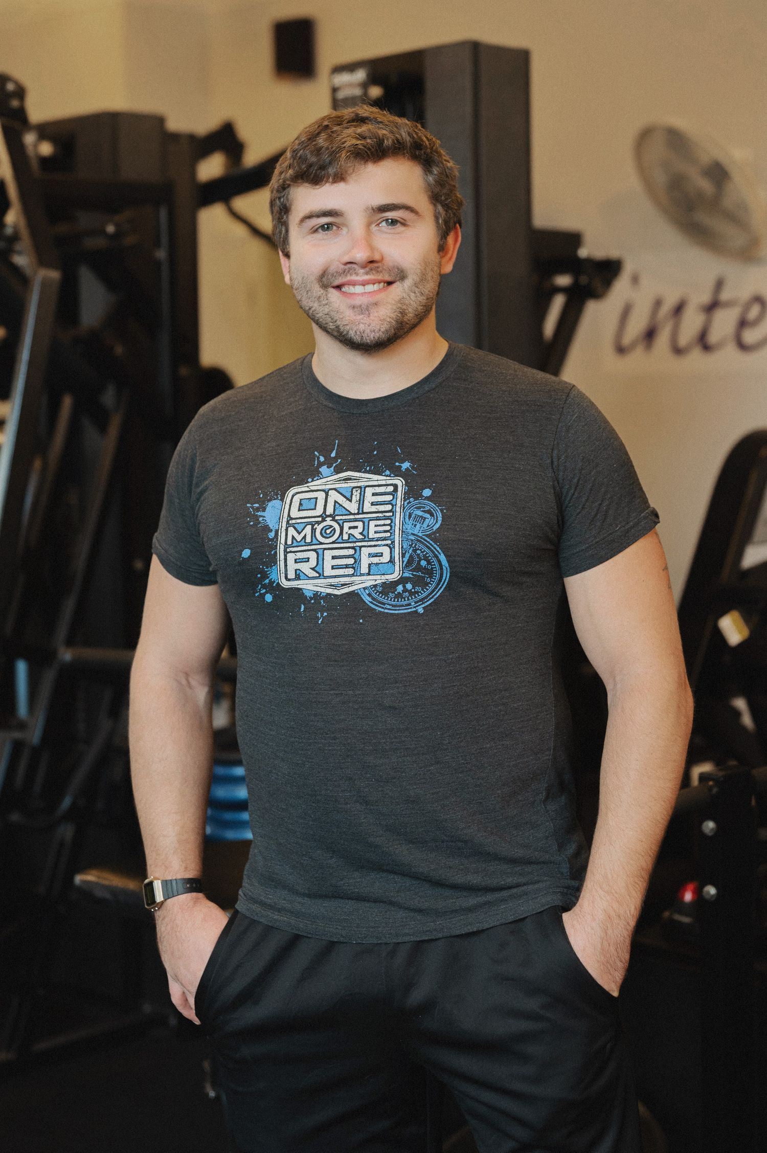Fitness instructor wearing dark t-shirt with logo standing in modern gym facility.