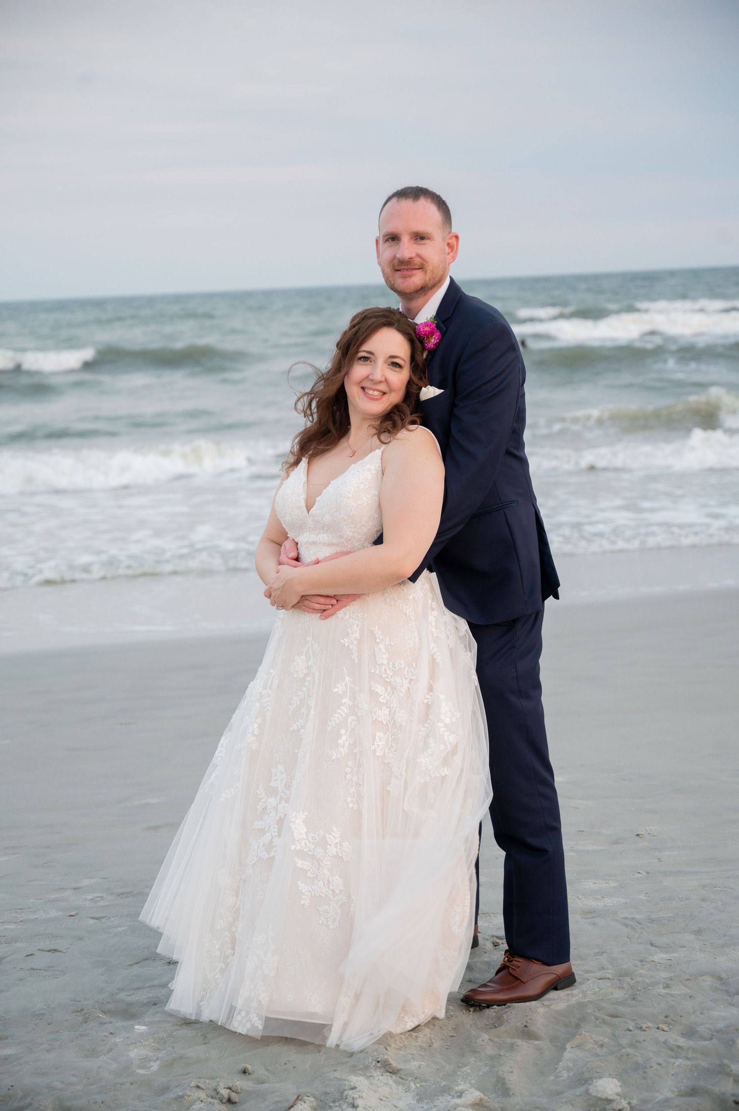 Couple poses for romantic photos along the shoreline with waves rolling in behind them.