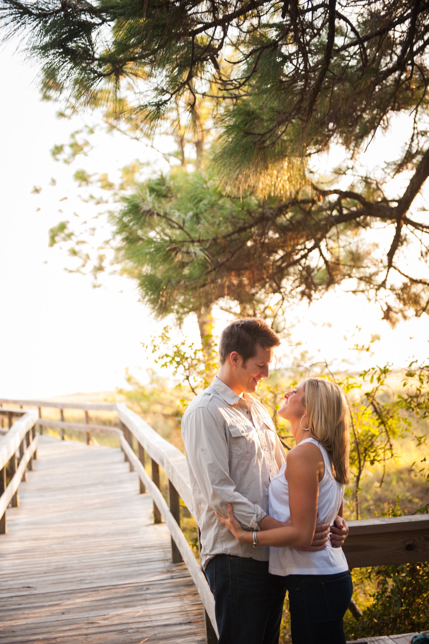 A couple embraces on a wooden deck at sunset surrounded by pine trees in a romantic outdoor setting.