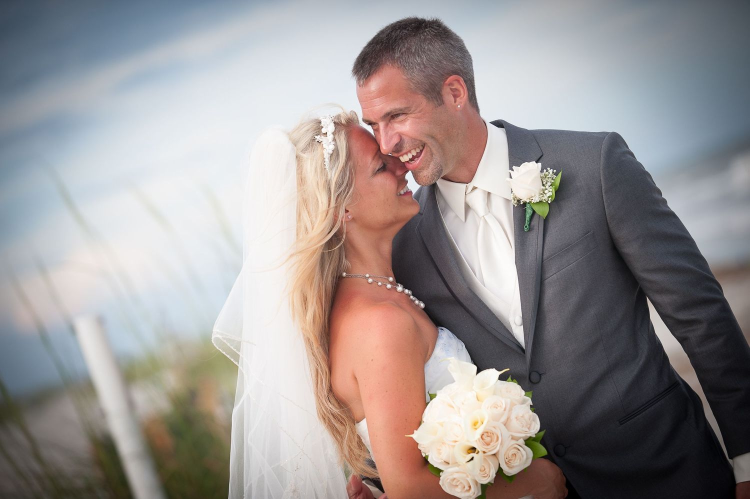 A romantic wedding Hilton Head couple embraces outdoors against a cloudy sky background with white floral bouquet details.