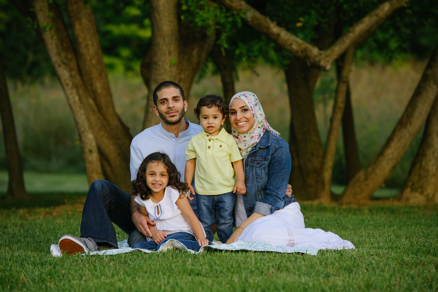 Family members sitting together and relaxing on green grass in a park during a sunny day.