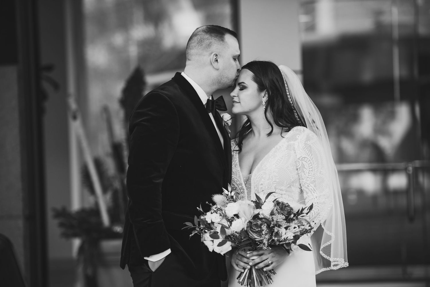 A romantic black and white wedding photo of a couple sharing an intimate moment while the bride holds a floral bouquet.
