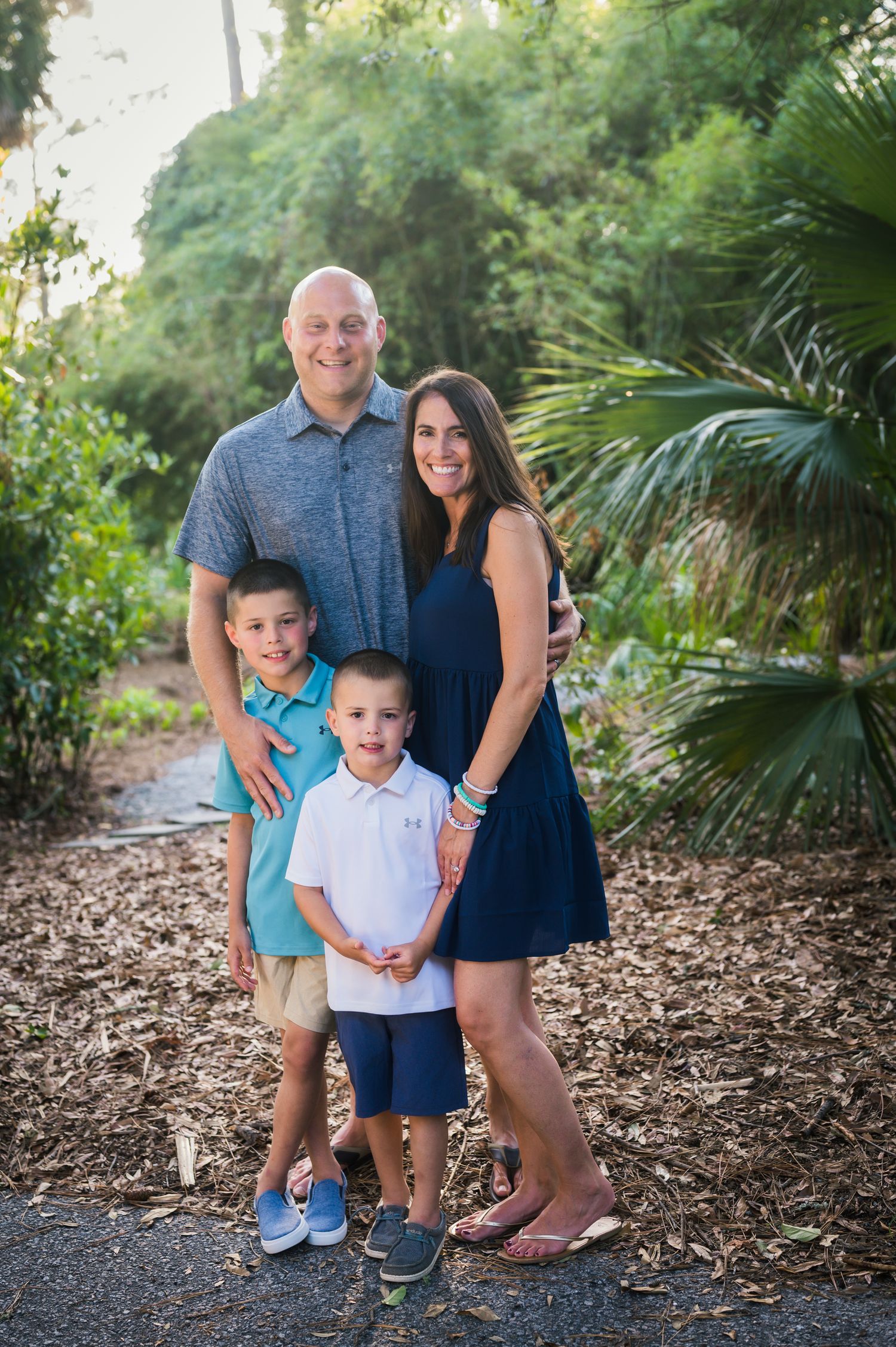 Family portrait session in lush garden setting with palm trees and mulch path.