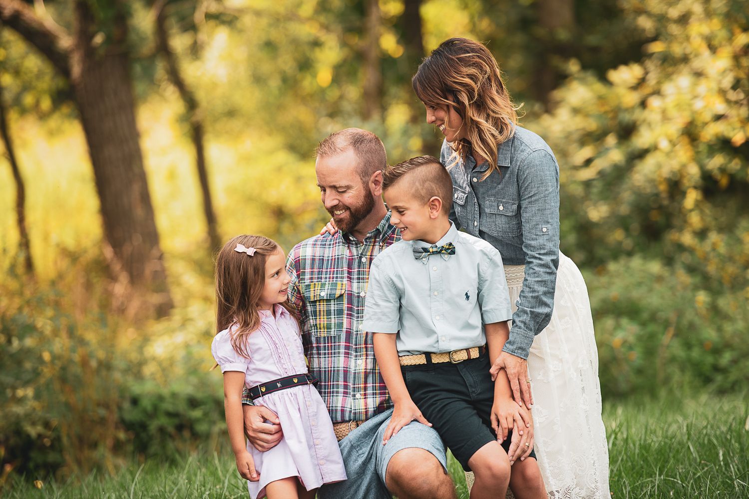 Family sitting together on grass in park during golden hour sunset with warm autumn lighting.