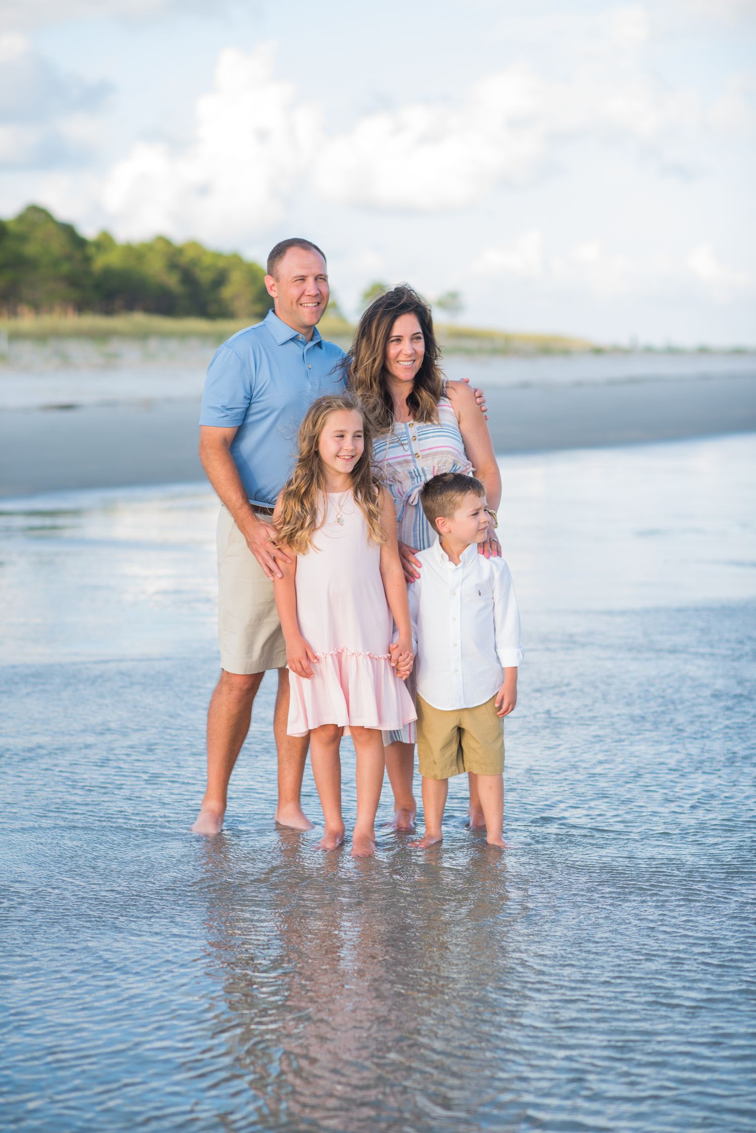 Family of four standing together in shallow ocean water during beach photoshoot. St. Augustine
