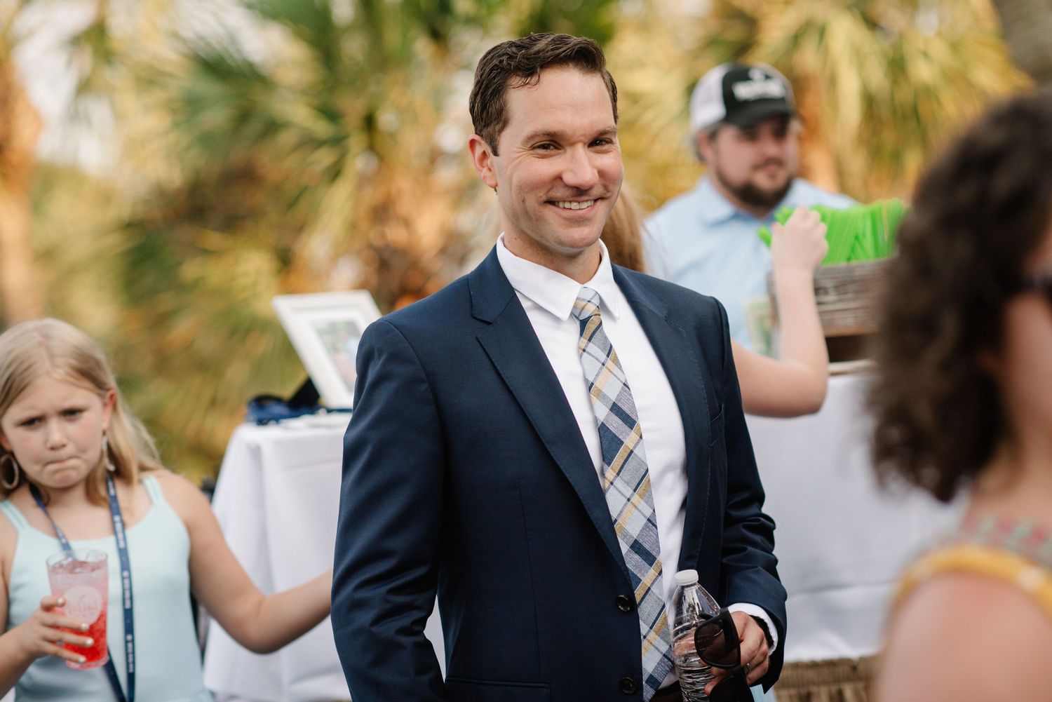 Wedding reception guests mingling outdoors under palm trees during daytime celebration. Hilton Head