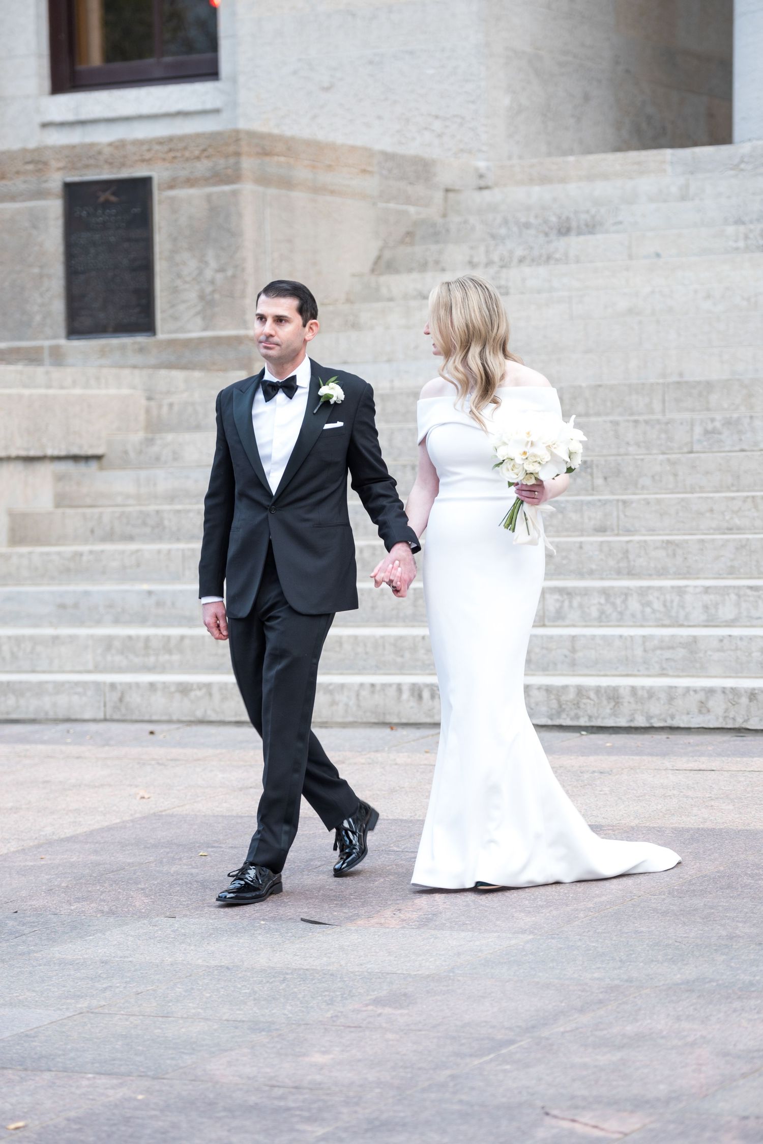 Elegant wedding couple poses playfully on outdoor steps in formal attire.