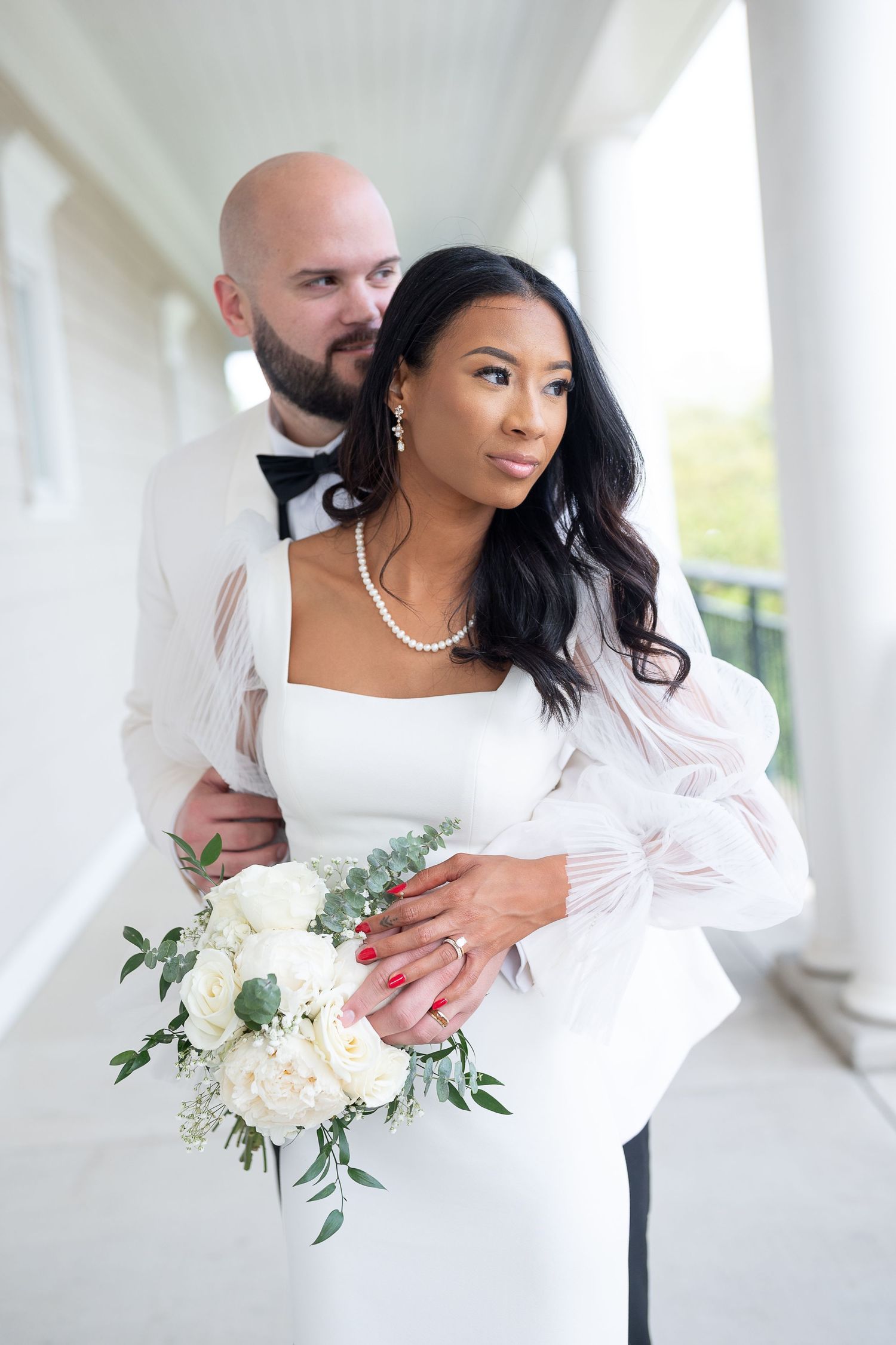 Elegant wedding couple embracing in white formal attire against classical columns.