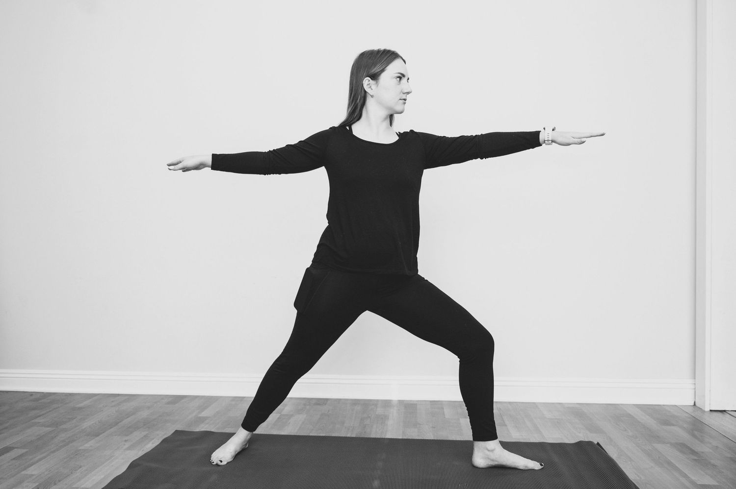 Person in black athletic wear demonstrating yoga warrior poses in a bright studio space.