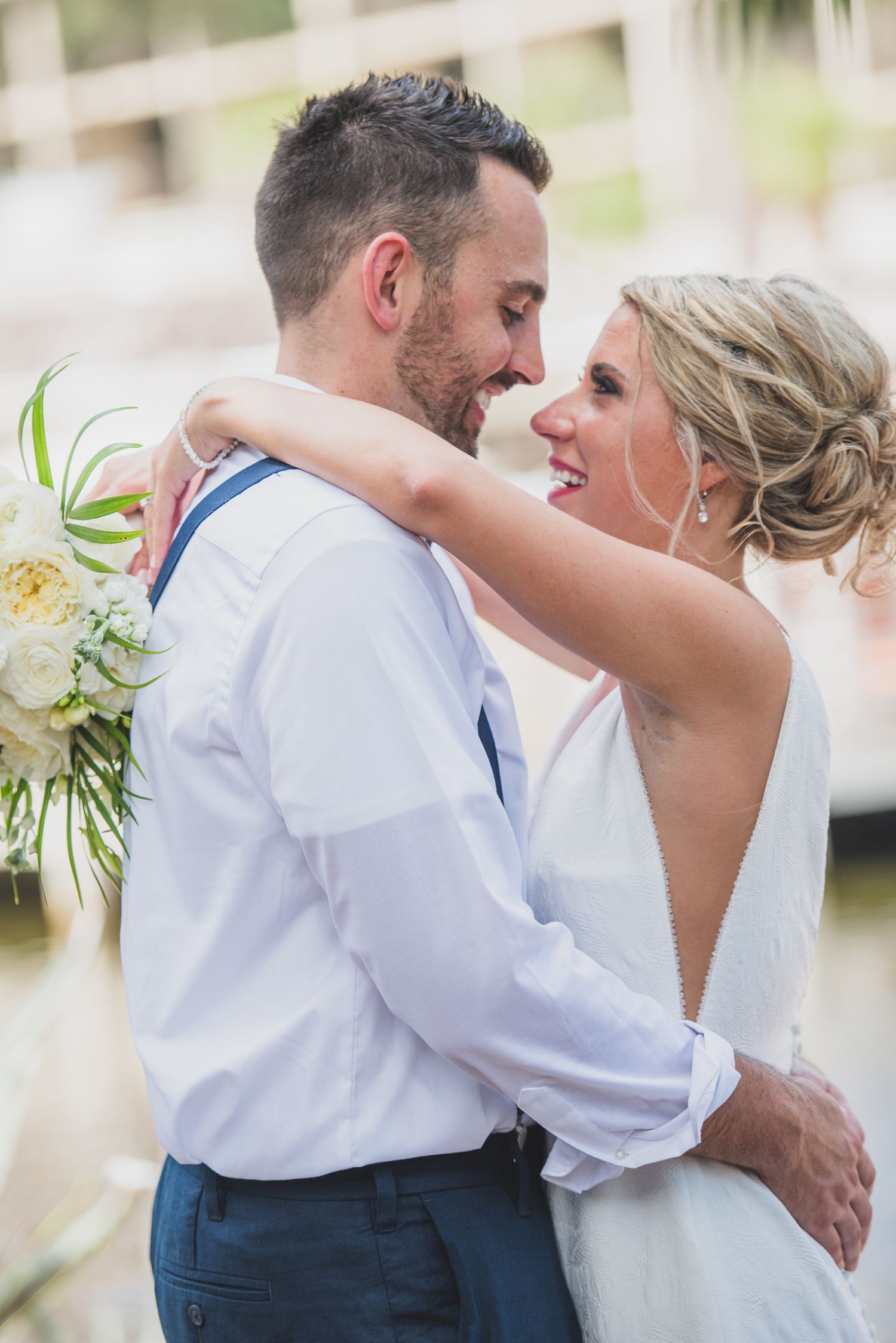 A romantic wedding couple embraces on a sunny day wearing white and navy attire.
