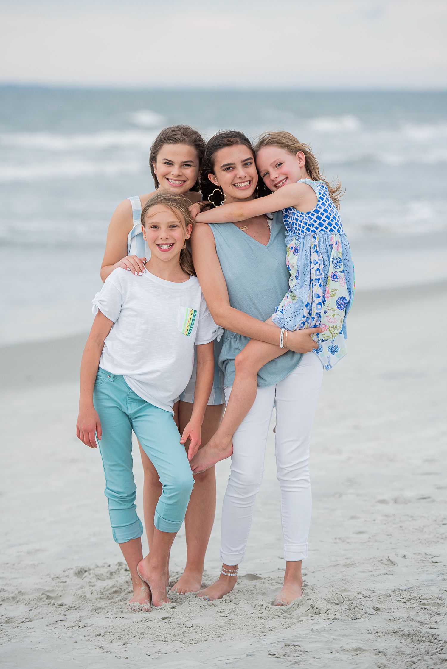 Family group poses together on a sandy beach at sunset with ocean waves in the background.