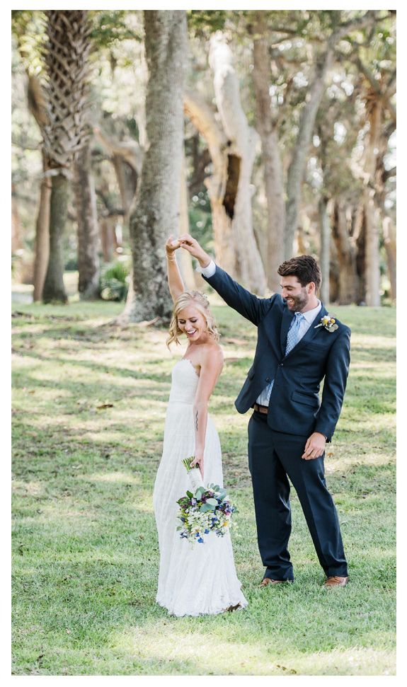A romantic wedding couple dances together under palm trees in a sun-dappled outdoor setting.