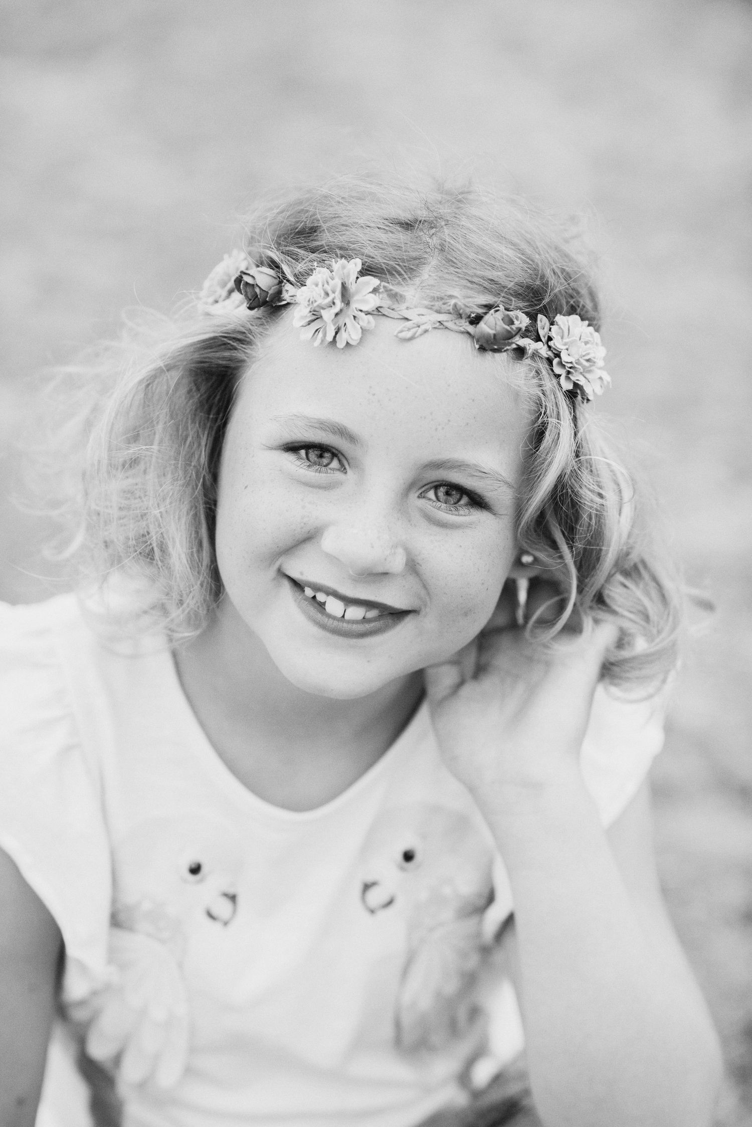 Black and white portrait series of a young child wearing a floral crown and white dress, smiling at the camera.