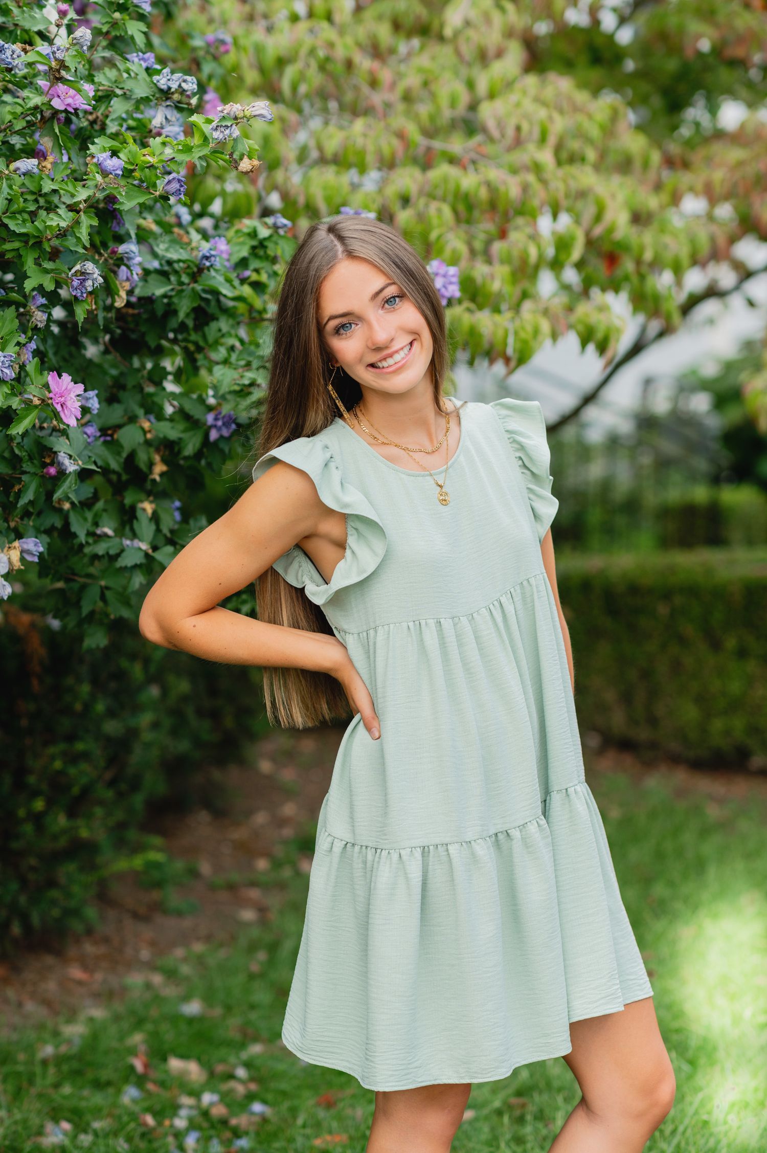 Light mint green ruffle top photographed against lush garden backdrop with purple flowers.