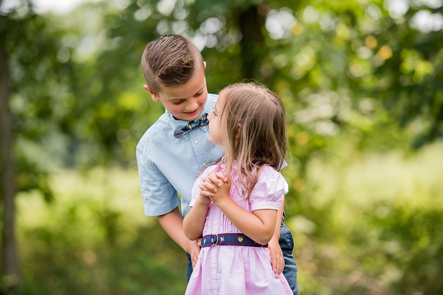 Two children in casual clothing share a tender moment while playing outdoors in a sunny garden setting.