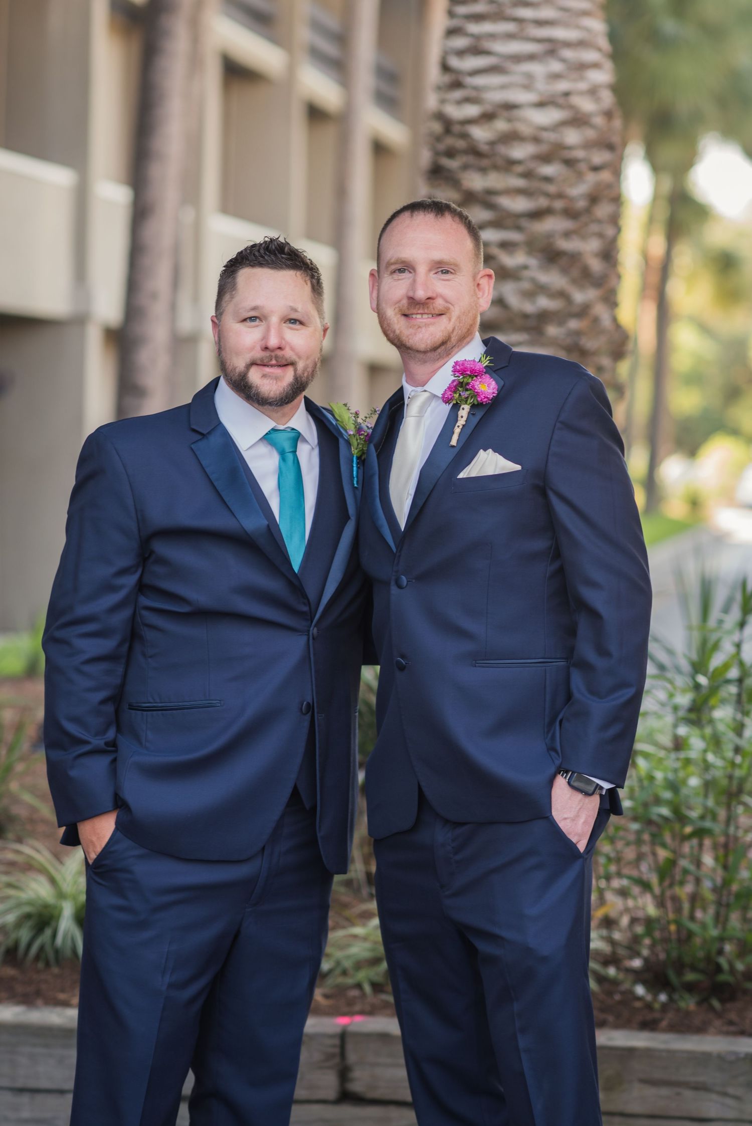 Groomsmen in navy suits with turquoise ties pose together outdoors near palm trees.