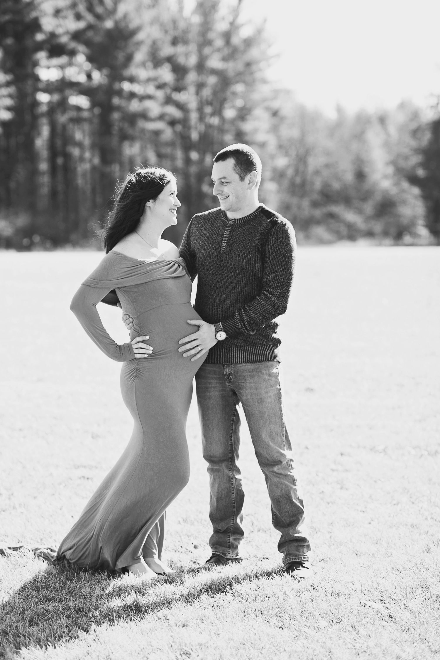 Black and white maternity photos of couple in casual wear on grassy field.