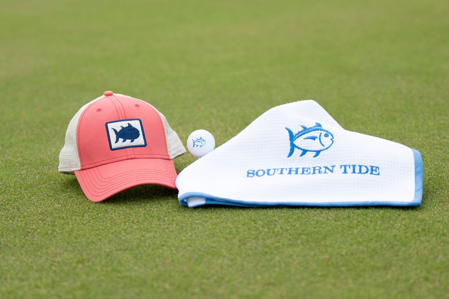 Southern Tide branded golf merchandise including coral hat and white headcover on green.