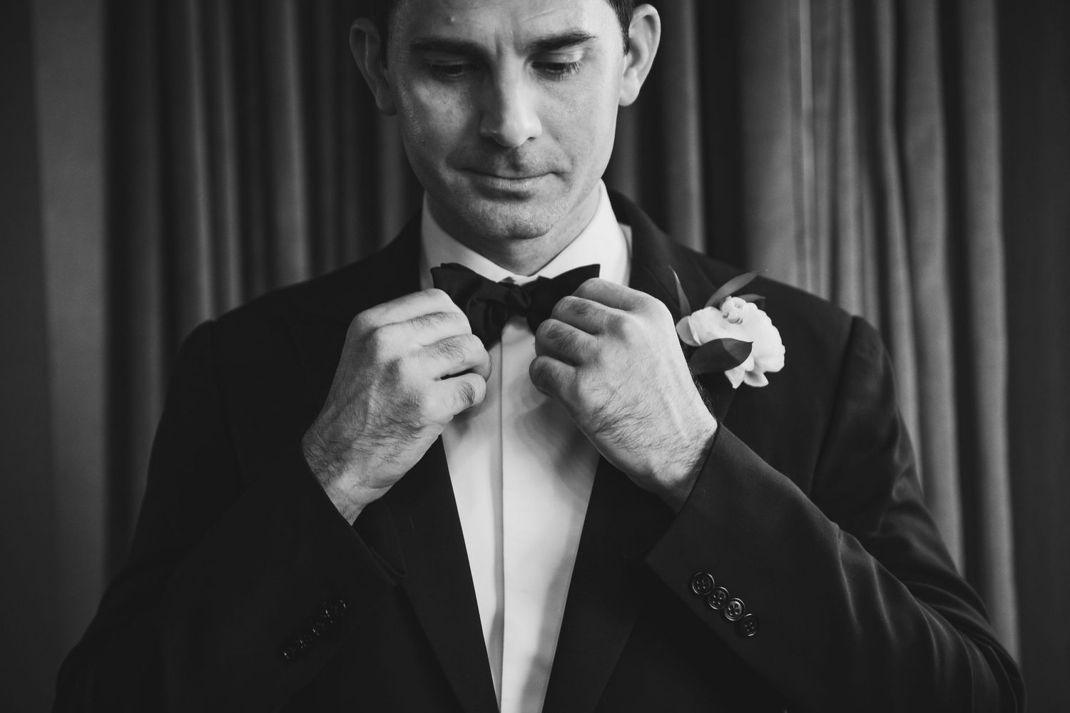 Black and white photo of formal attire preparation with bow tie and boutonniere.