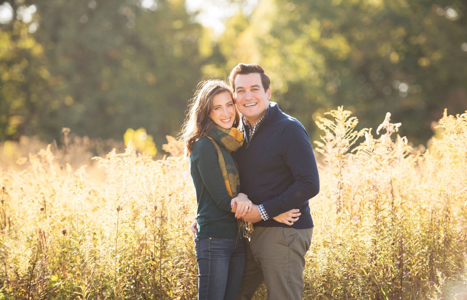 A romantic couple embraces in a golden sunlit field of tall grass during sunset.