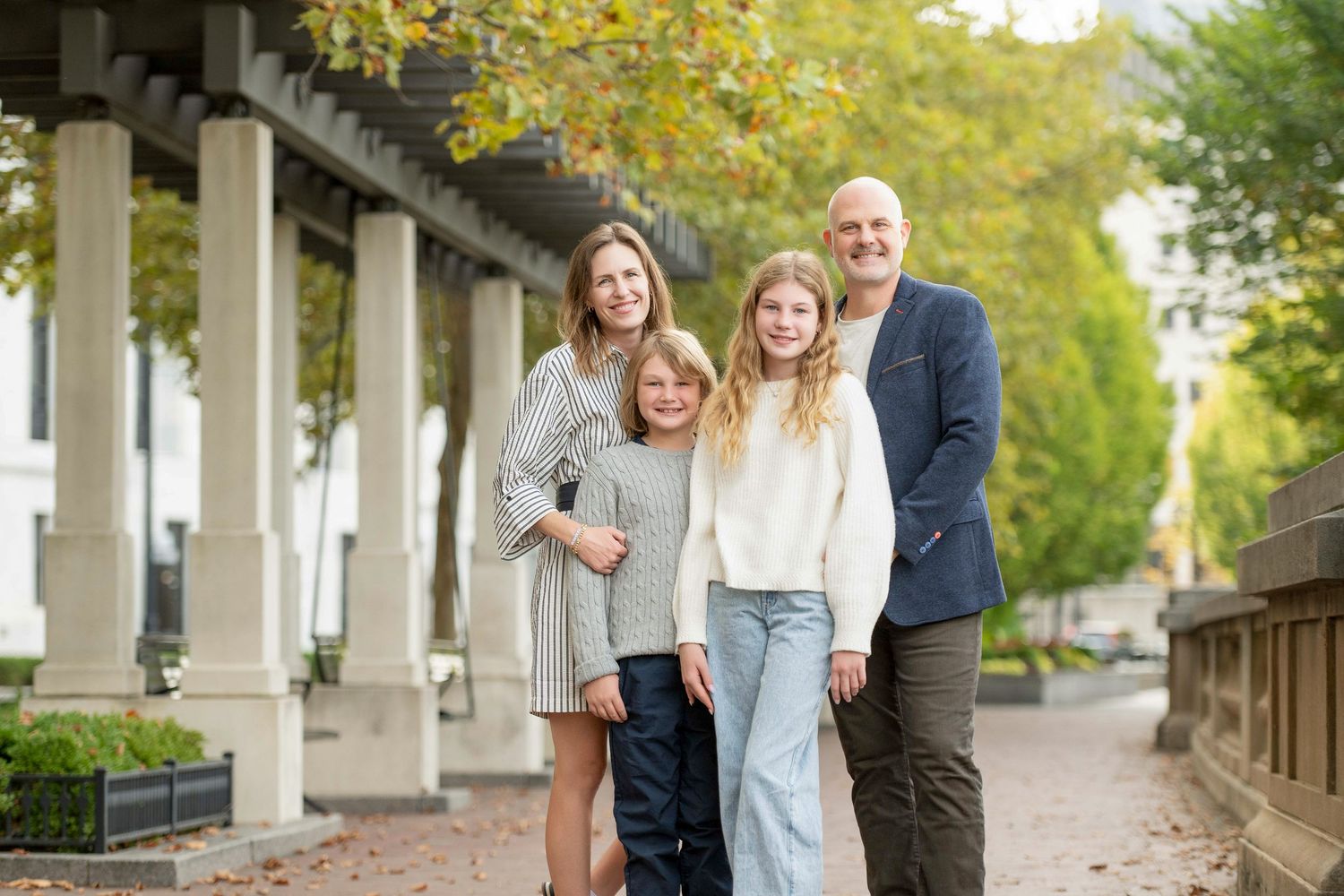 Family of four poses together on tree-lined walkway during autumn. St. Augustine Beach, Hammock Beach photographer.