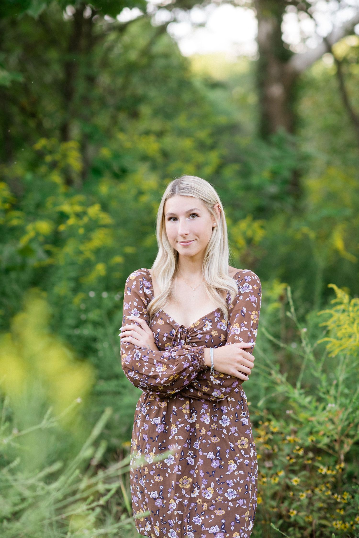 A brown floral dress is worn in an outdoor garden setting with green foliage in the background.