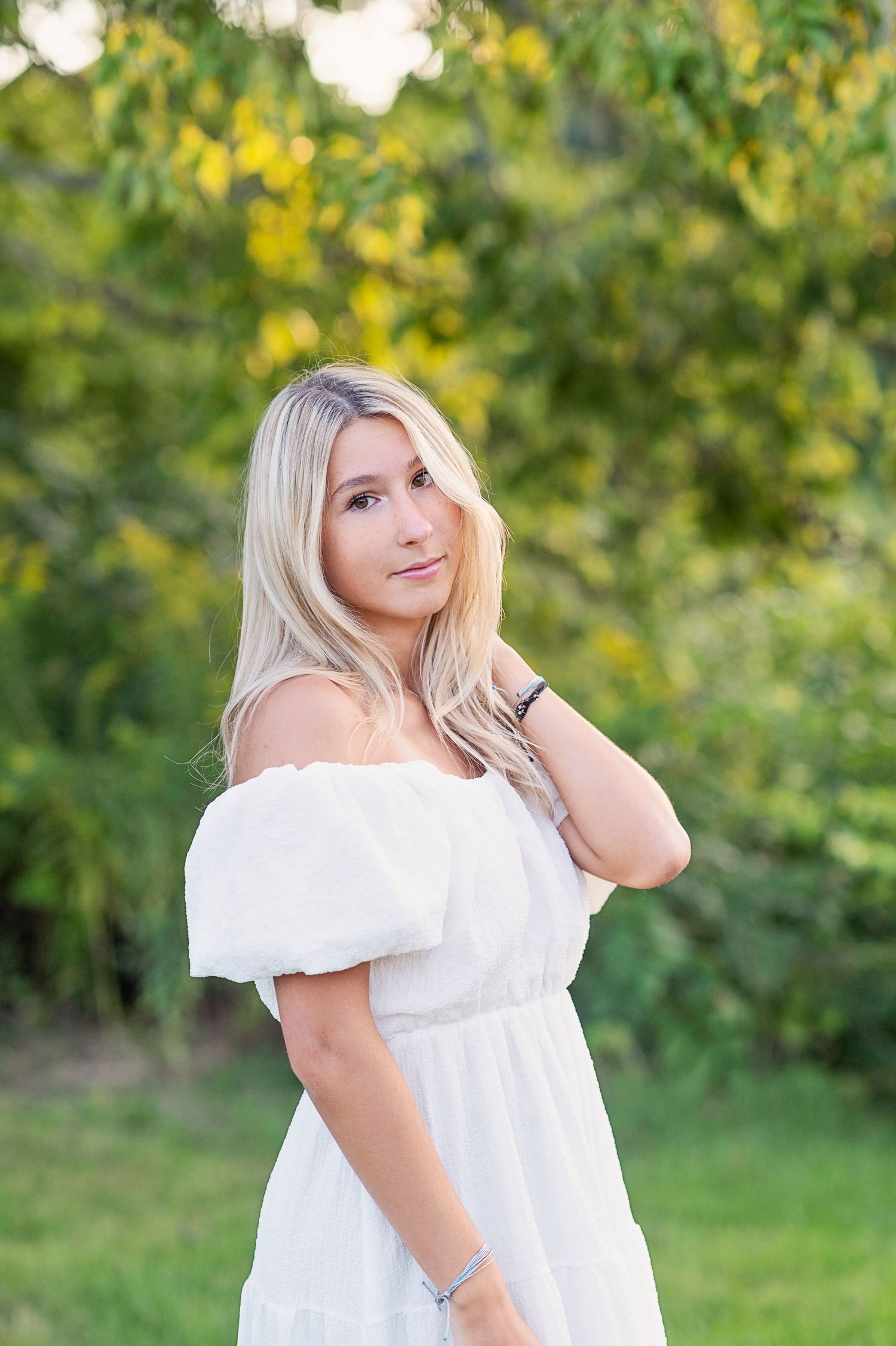 A romantic portrait featuring an off-shoulder white dress against a lush green background.