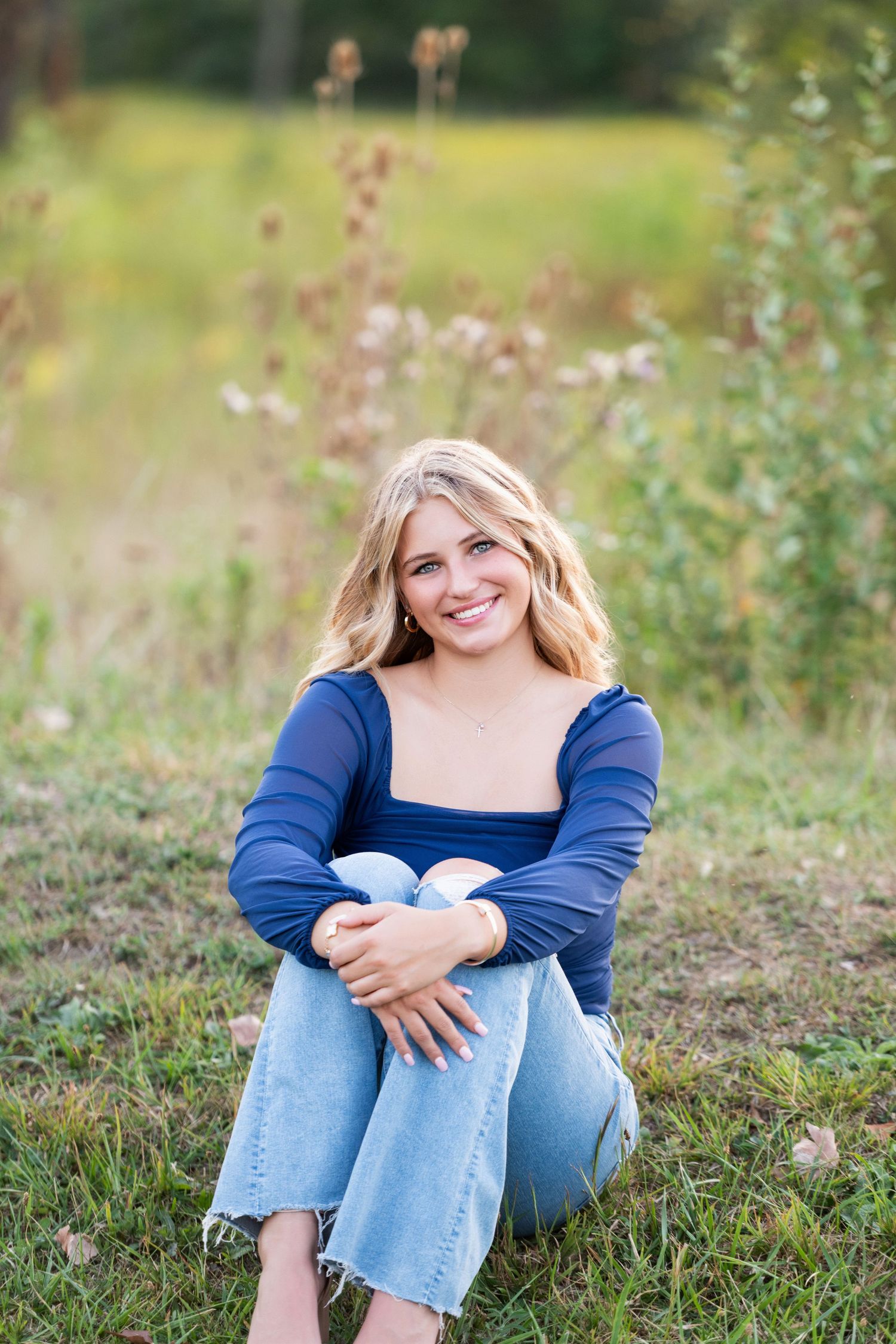 A series of outdoor portrait photos showing someone in a blue top and jeans sitting casually in green grass.