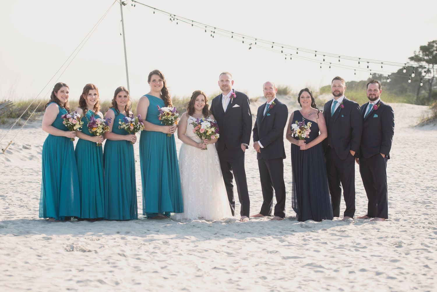Beach wedding ceremony setup with string lights and guests in formal attire.