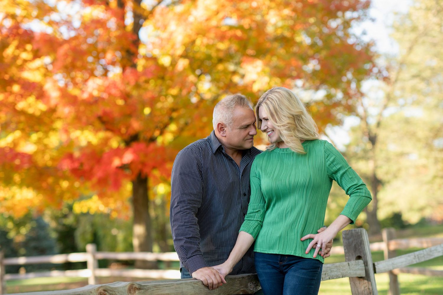 Couple sharing intimate moments with beautiful fall colors and wooden fence in background.