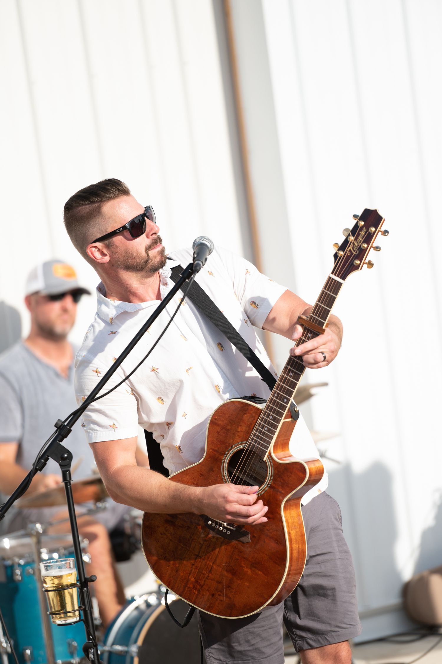 Musician in sunglasses and white t-shirt performs with acoustic guitar in bright studio setting.