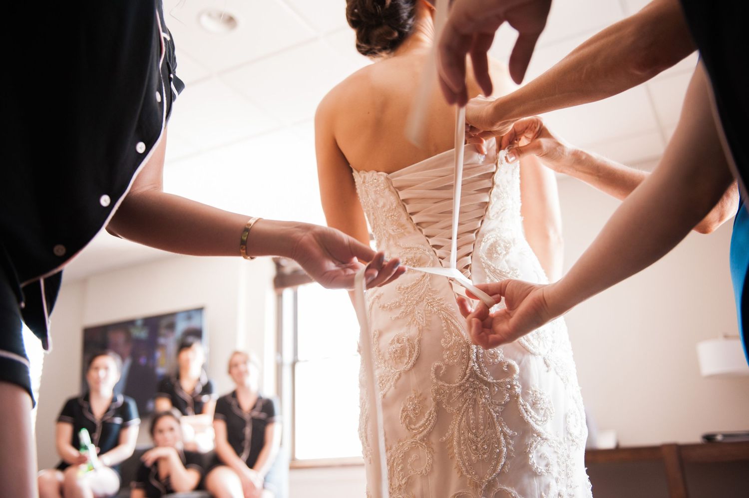 Wedding dress details being adjusted and laced up in warm natural lighting during bridal preparations.