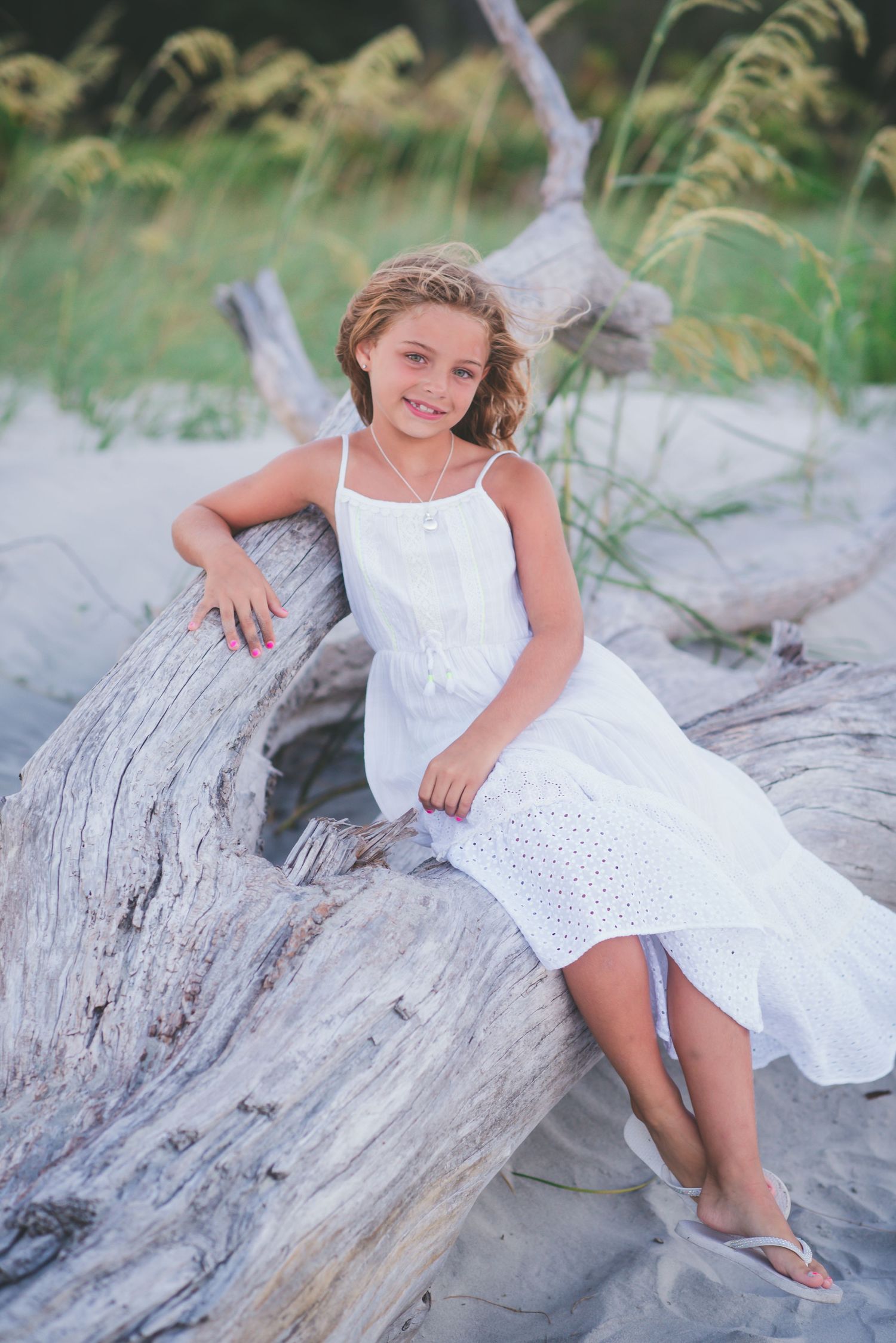 Child relaxing on driftwood at the beach wearing a white eyelet dress. St. Augustine