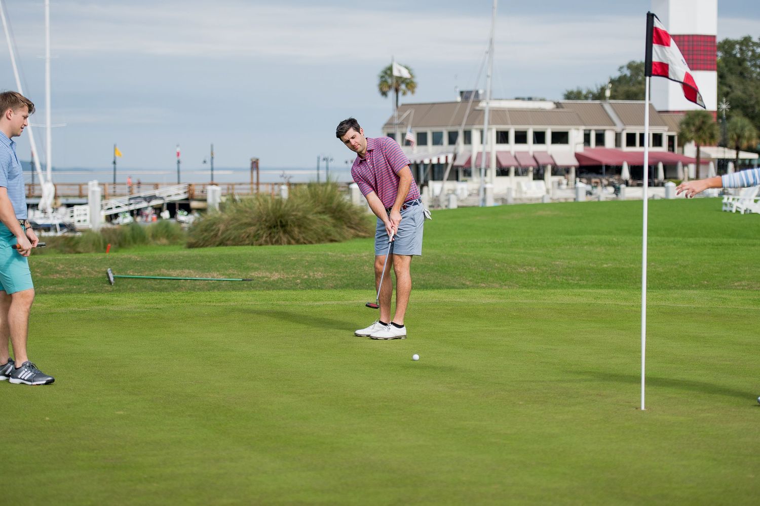 Golfer putting on green with flag and clubhouse in background. Sea Pines Hilton Head