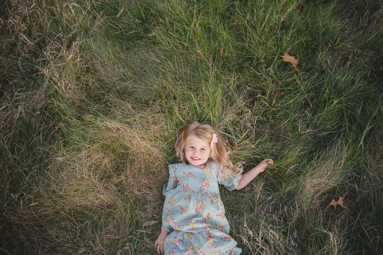 A young child in a blue dress plays in a field of tall grass while rolling and moving through the grass.