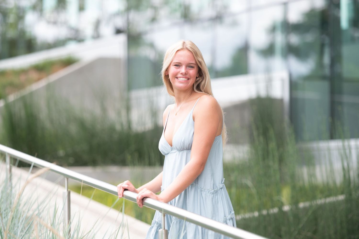 A woman in a light blue dress poses outdoors near modern glass architecture.