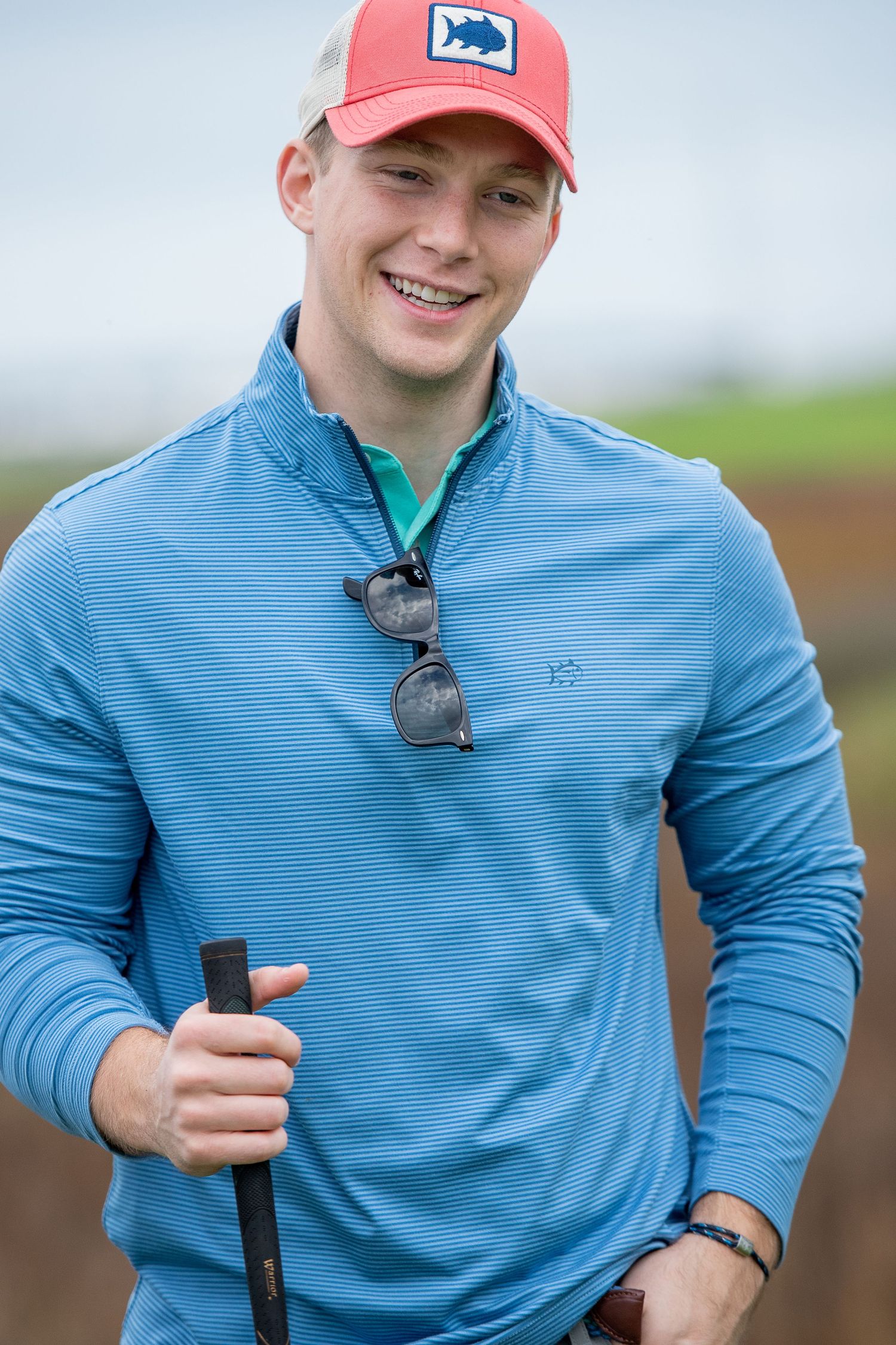 Golfer wearing blue striped pullover and coral hat poses with golf club on course. Sea Pines Hilton Head. Southern Tide Brand editorial phot