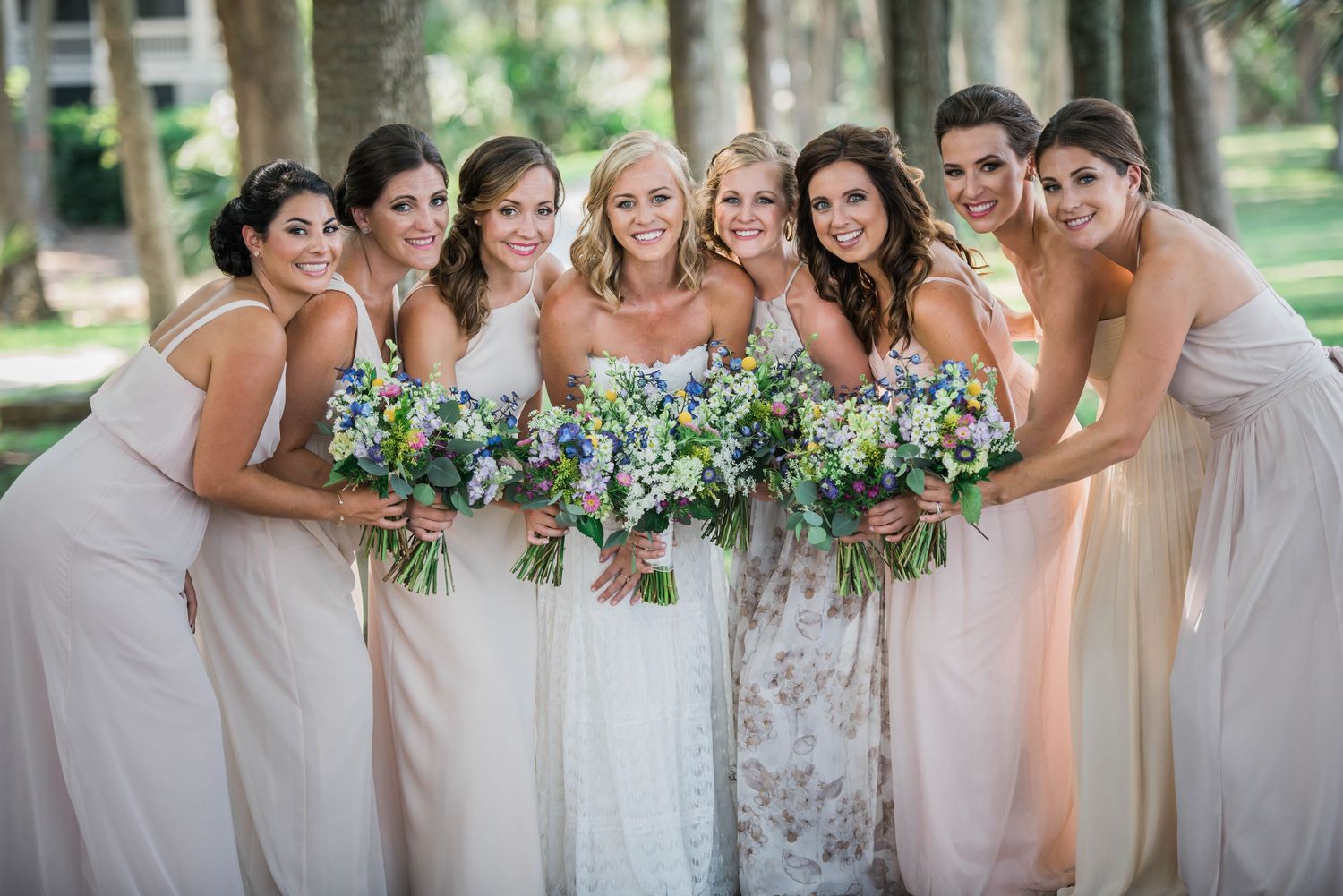 Hilton Head Bridesmaids in blush pink dresses pose together with bouquets in an outdoor garden setting.