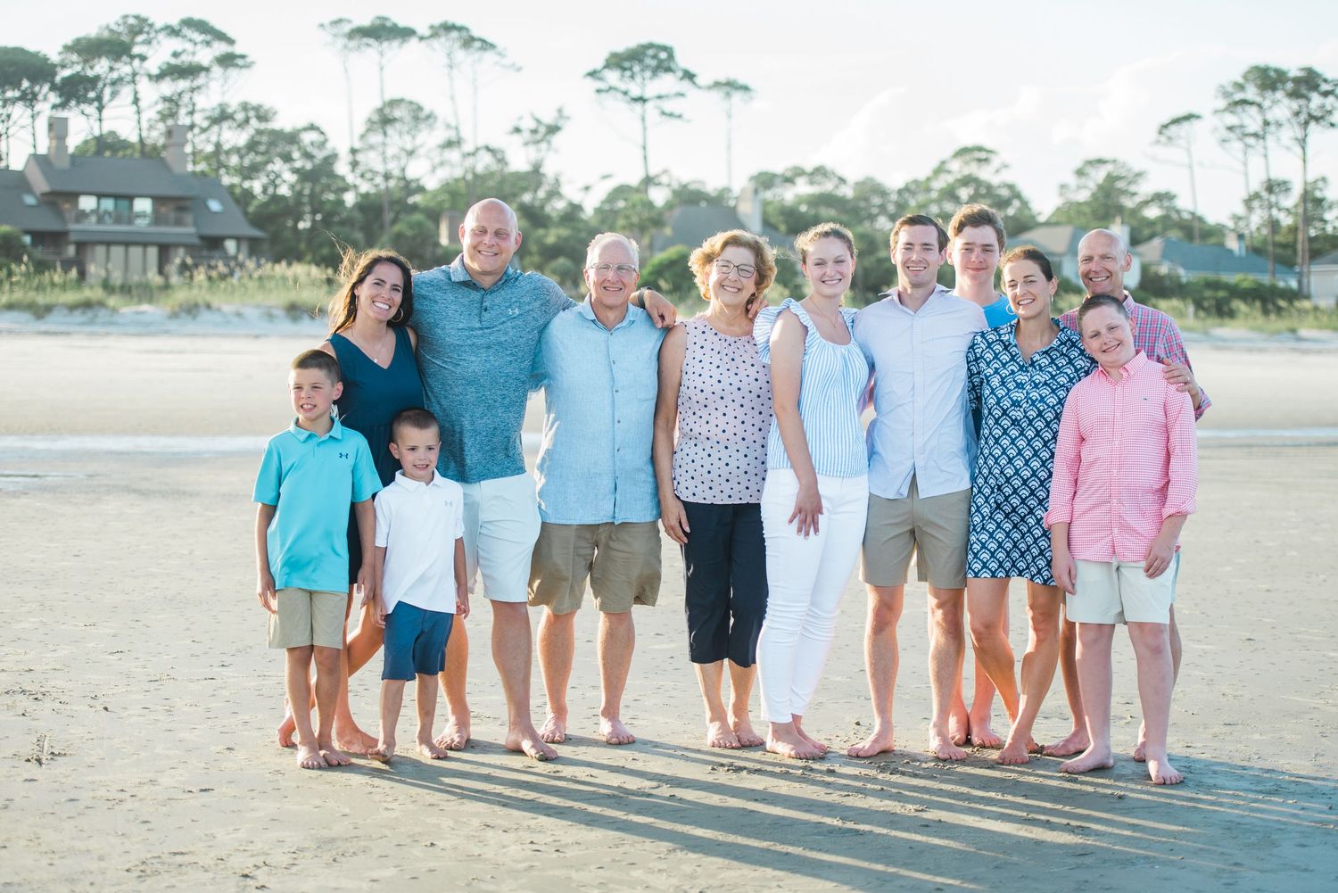 Extended family wearing coordinated blue and white outfits poses together on beach with palm trees.