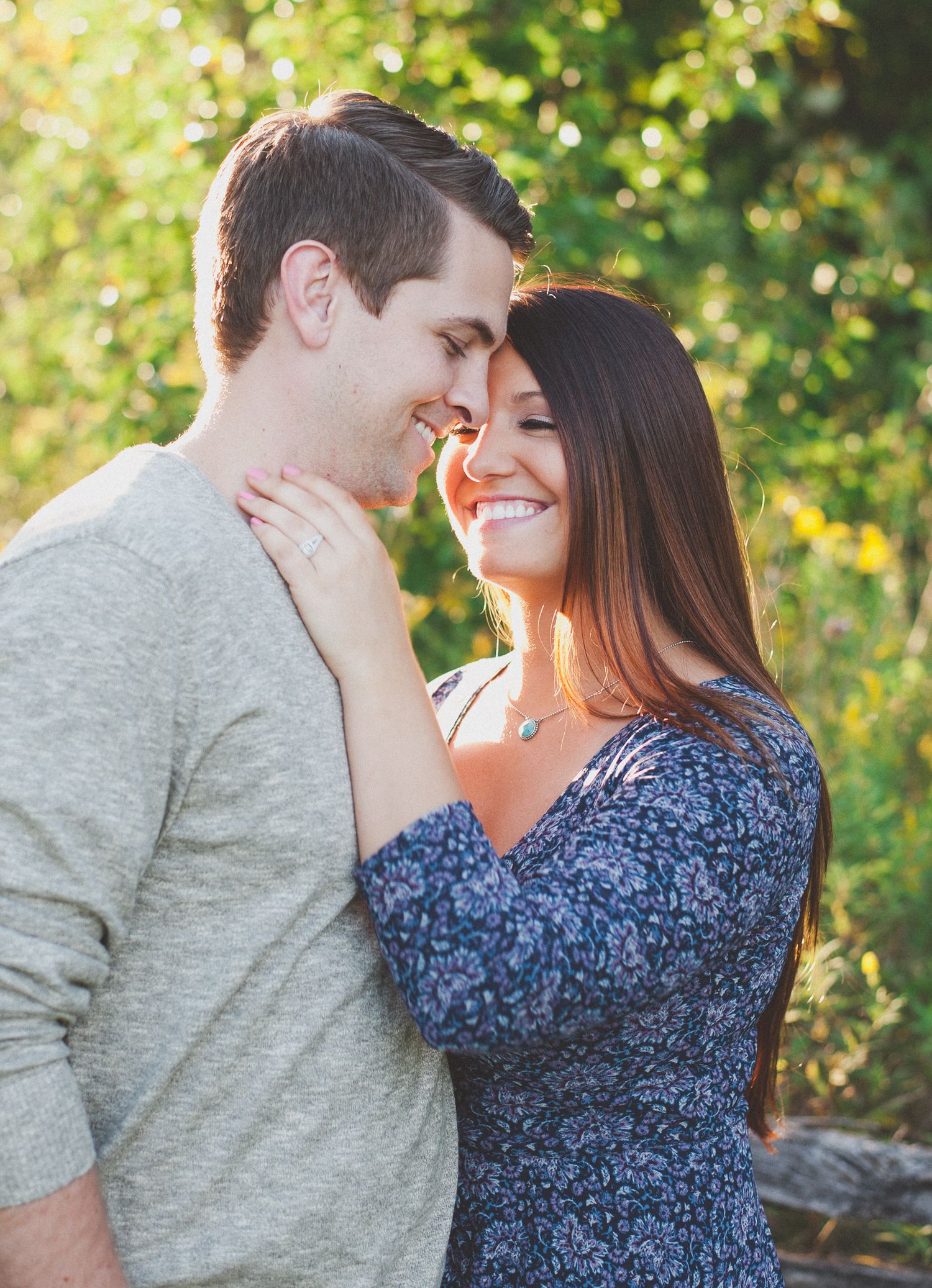 Couple shares tender moments in a natural outdoor setting with green foliage in background.