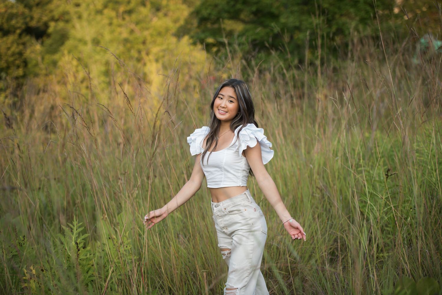 Person in white dress twirls playfully in a sunlit field with tall grass.