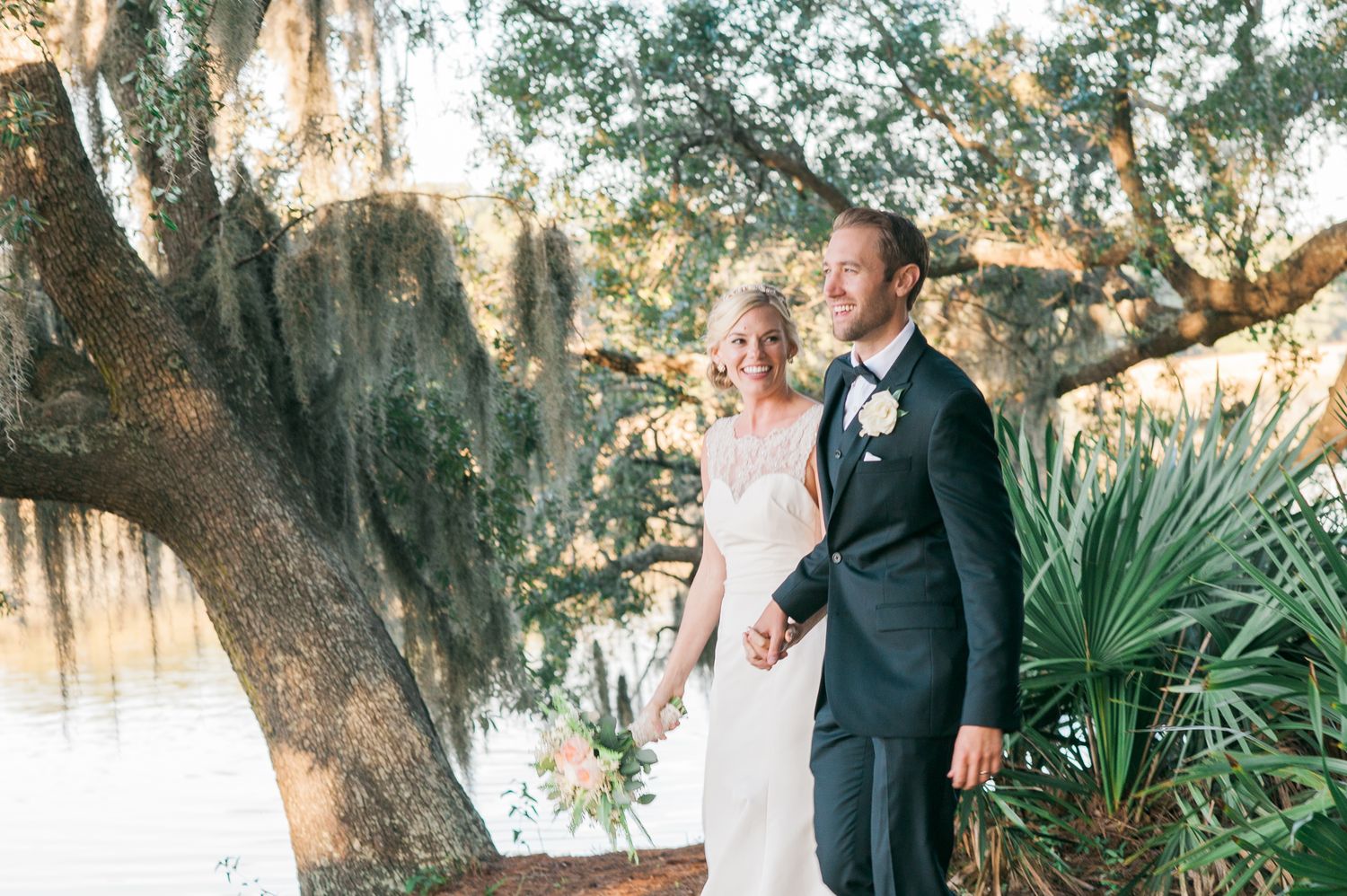 A newlywed couple stands together under Spanish moss draped trees near a waterfront. Hammock Beach engagement session.
